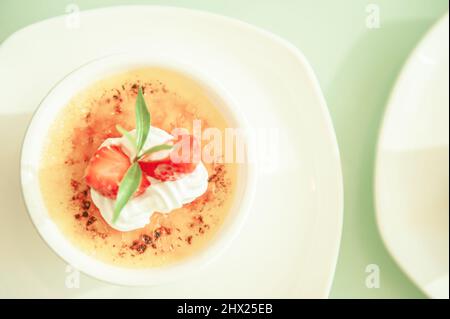 crème Brulee oder Burnt Cream mit Erdbeere auf einer weißen Tasse, weiß verschwommen im Hintergrund. Nahaufnahme. Draufsicht. Stockfoto