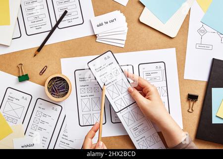 UI / UX Front-End-Designer arbeitet an mobilen responsive Website. Flaches Bild mehrerer App-Drahtgardeskizzen über dem Schreibtisch des Produktdesigners. Stockfoto