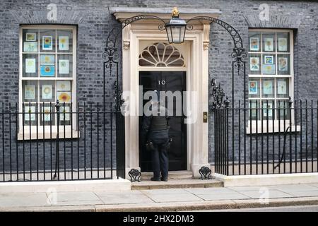 London, Großbritannien, 8.. März 2022. Ein Polizist, der die Downing Street Nr. 10 betreten hat, deren Fenster mit Zeichnungen von Sonnenblumen geschmückt sind, der Nationalblume der Ukraine in Solidarität mit dem belagerten Land. Stockfoto