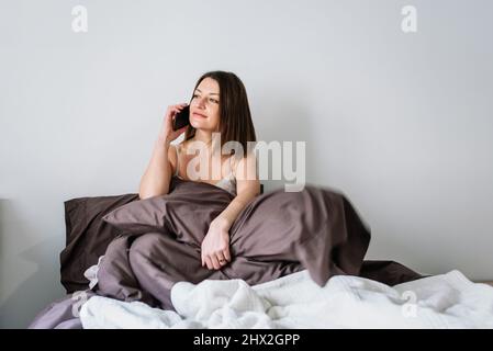 Frau, die im Bett sitzt und am Telefon telefoniert. Stockfoto