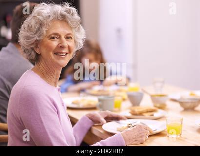 Der beste Start in den Tag. Beschnittenes Porträt einer älteren Frau, die mit ihrer Familie das Frühstück genießt. Stockfoto