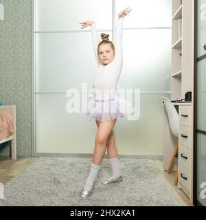 Eine kleine Ballerina im weißen Badeanzug tanzt zu Hause, lernt aus der Ferne tanzen. Tanzunterricht zu Hause Stockfoto