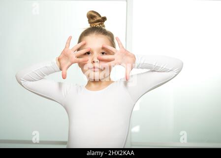 Porträt einer kleinen hübschen Blondine, während sie in einem weißen Badeanzug tanzt. Lateinamerikanischer Tanzkurs Stockfoto