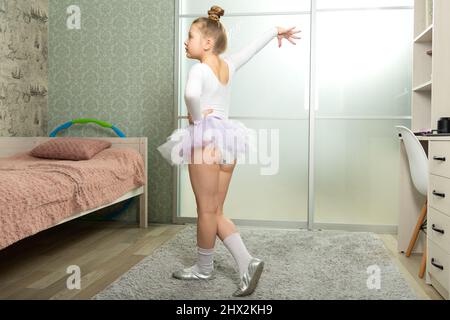 Eine kleine Ballerina im weißen Badeanzug tanzt zu Hause, lernt aus der Ferne tanzen. Tanzunterricht zu Hause Stockfoto