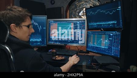Männliche Händler, Freiberufler an der Börse, tradet Optionen und isst Nüsse Stockfoto