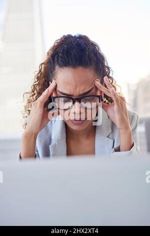 Eine junge Frau sitzt mit Kopfschmerzen an ihrem Computerbildschirm im Stadtbüro Stockfoto
