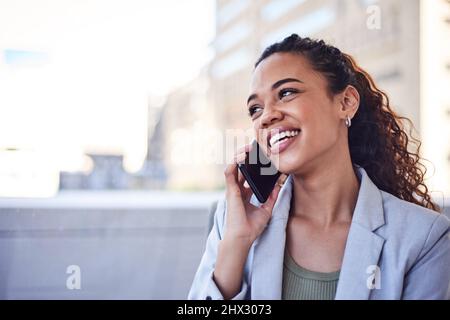 Eine junge Frau mit lockigen Haaren redet und lacht am Telefon mit der Stadt dahinter Stockfoto