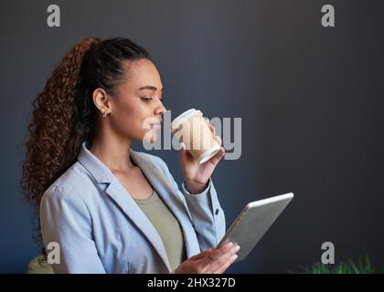 Eine junge Frau schlisst ihren Kaffee zum Mitnehmen und ihr digitales Tablet, das für den Tag vorbereitet ist Stockfoto