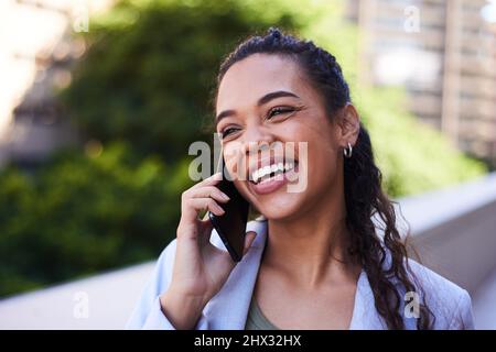 Eine junge Frau lächelt und lacht, während sie draußen auf einem Balkon telefoniert Stockfoto