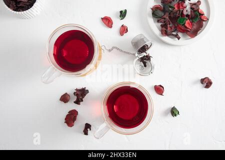 Zwei transparente Glas-Tassen Hibiskus roten Tee auf weißem Hintergrund mit getrockneten Rosenblättern. Draufsicht. Das Konzept der Gewichtsabnahme Stockfoto