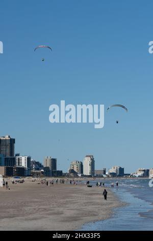 Im Winter fliegen zwei motorbetriebene Gleitschirme über den Strand von South Padre Island, Texas. Auf einem elektrisch betriebenen Paraglicer trägt der Pilot einen Rucksackmotor. Stockfoto