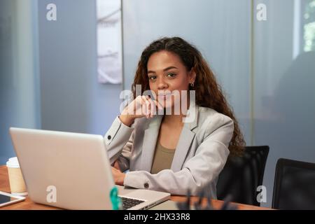 Eine junge Frau sitzt an ihrem Schreibtisch in einem Firmenbüro vor ihrem Laptop Stockfoto