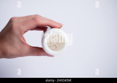 Weibliche Hand mit einer Flasche weißer Tabletten auf hellem Hintergrund. Selektiver Fokus in der Flasche auf Pillen. Stockfoto