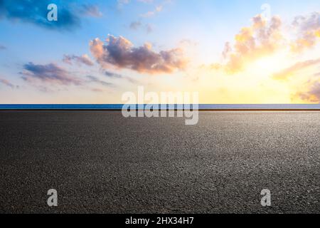 Leere Asphaltstraße und See mit farbenfroher Wolkenlandschaft bei Sonnenuntergang Stockfoto