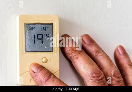 Ein älterer, älterer, alter Mann passt die Temperatur seines Heims über einen digitalen Thermostat an, wenn die Heizkosten steigen. Stockfoto