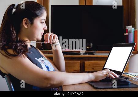 Seitenansicht einer jungen kaukasischen Frau, die zu Hause sitzt und Daten und Statistiken auf ihrem Computer in ihrem Heimbüro analysiert, Unternehmerin Conce Stockfoto