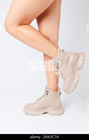 Weibliche Beine in beigefarbenem Leder Schuhe aus der neuen Kollektion auf weißem Hintergrund weibliche Beine in modischen Schuhen aus Kunstleder Frühjahr 2022. Stockfoto