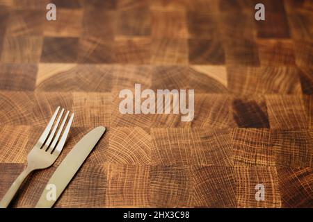 Eine goldene Gabel und ein Messer, die auf einer leeren Ablagefläche eines Metzgerblocks in einer Küche sitzen Stockfoto