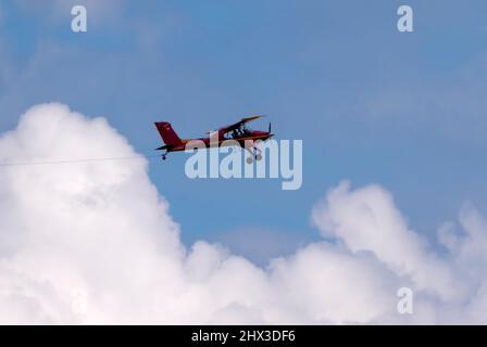 Rotes kleines Sportflugzeug, das in den Himmel fliegt, zieht am Seil das Segelflugzeug. Stockfoto