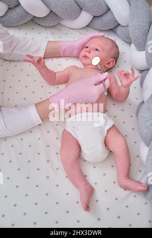 Ein Arzt in Uniform überprüft den Mund eines Kindes mit einem Spiegel. Der Zahnarzt untersucht die Zähne eines Neugeborenen Stockfoto