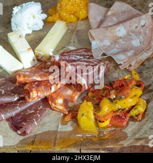 Köstliche Antipasto-Auswahl an Fleisch und Käse mit gerösteten Paprika auf einem Holzbrett im quadratischen Format selektiven Fokus Stockfoto