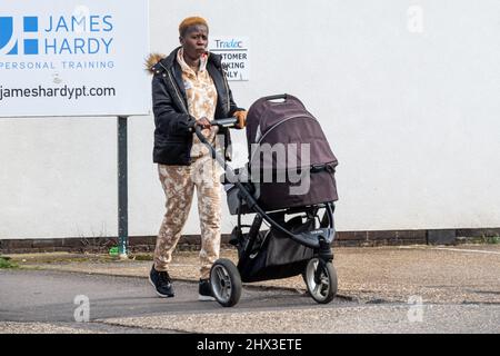 Junge schwarze oder afrikanische Mutter, die die Straße entlang geht und ihr Baby in einen Kinderwagen schiebt, Großbritannien Stockfoto