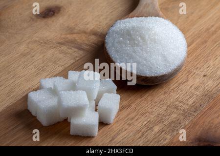 Granulatzucker und Zuckerwürfel in Holzlöffel auf Holzboden Stockfoto