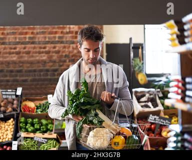 Ich will nur das frischeste. Aufnahme eines jungen Mannes, der in einem Supermarkt mit einem Korb voller frischer Produkte läuft. Stockfoto