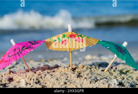 Drei kleine Papier-Cocktail-Schirme stehen im Sand am Sandstrand aus nächster Nähe Stockfoto