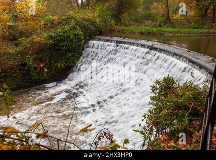 Das historische gekrümmte Wehr am Fluss Bollin in der Steinbruch-Bank-Mühle in Styal Chesshire mit dem Mühlentool über dem Wehr Stockfoto