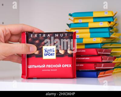 Tambow, Russische Föderation - 19. Februar 2022 Frau nimmt Ritter Sport Haselnuss-Schokoriegel aus dem Regal des Küchenschranks Stockfoto