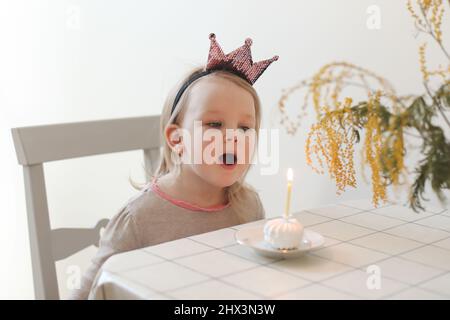 Nettes kleines Mädchen bläst Kerze auf einem Geburtstagskuchen zu Hause aus. Geburtstag des Kindes Stockfoto