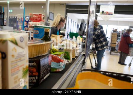 Lebenshaltungskosten Lebensmittel an der Kasse Co Op Supermarktarbeiterin Frau, die an der Kasse arbeitet und eine Covid-Maske trägt Wales 2022 KATHY DEWITT Stockfoto