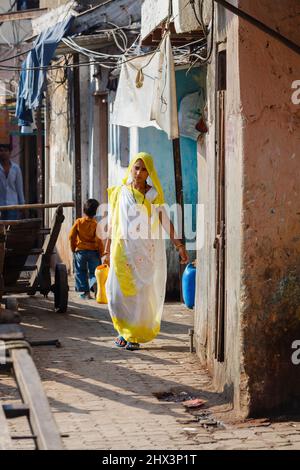 Eine junge Frau in gelber und weißer einheimischer Kleidung mit verdecktem Kopf geht durch eine Gasse in Mahalaxmi Dhobi Ghat, einer Open-Air-Wäscherei in Mumbai, Indien Stockfoto