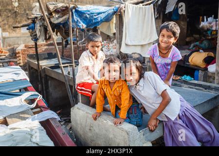 Einheimische Kinder, Jungen und Mädchen spielen glücklich unter dem Trocknen von Kleidung auf einem Waschstift in Mahalaxmi Dhobi Ghat, einer großen Open-Air-Wäscherei in Mumbai, Indien Stockfoto