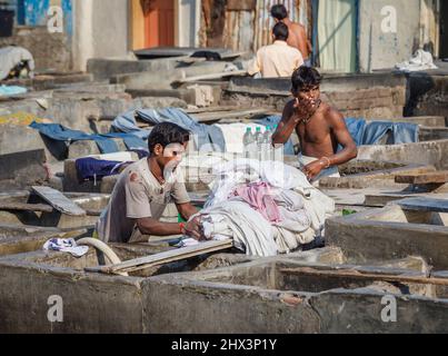 Ein Dhobi Wallah (Washerman) arbeitet in Mahalaxmi Dhobi Ghat, einem großen Open-Air-Waschsalon in Mumbai, Indien, mit einem typischen Betonwaschstift Stockfoto