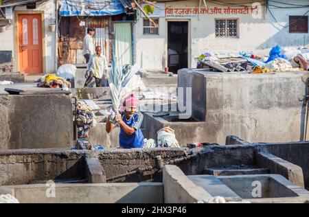 Ein Dhobi Wallah (Washerman) arbeitet Waschmittel in einem typischen Betonwaschstift in Mahalaxmi Dhobi Ghat, einem großen Open-Air-Waschsalon, Mumbai, Indien Stockfoto