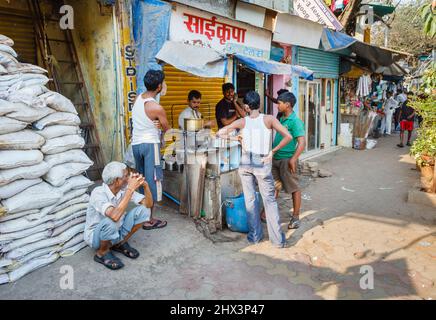 Einheimische Männer versammeln sich um einen Lebensmittelverkäufer auf der Straße und ein Mann hockt neben Lebensmittelsäcke vor Mahalaxmi Dhobi Ghat, einer großen Open-Air-Wäscherei in Mumbai, Indien Stockfoto