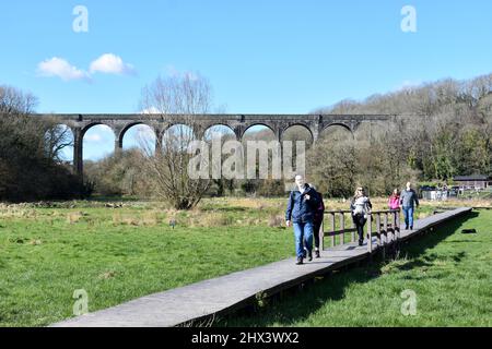 Menschen, die auf der Holzpromenade im Porthkerry Country Park vor dem Eisenbahnviadukt spazieren, Barry, Glamorgan, Wales Stockfoto