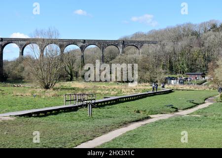 Menschen, die auf der Holzpromenade im Porthkerry Country Park vor dem Eisenbahnviadukt spazieren, Barry, Glamorgan, Wales Stockfoto