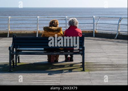 Ältere Menschen sitzen in der Wintersonne auf einer Bank auf einem Norfolk Pier Stockfoto