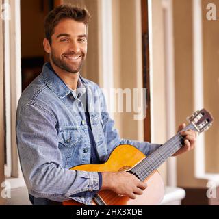 Lasst mich Euch ein Lied spielen. Porträt eines hübschen jungen Mannes, der sich auf der Terrasse entspannt, während er eine Gitarre spielt. Stockfoto