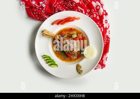 Geschmorte Lamb Shanks mit Sauce und Tomaten, Gurken, Rettich in einem Gericht isoliert auf bunten Tischtuch Draufsicht auf grauem Hintergrund Stockfoto