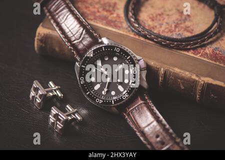 Herren Accessoires auf schwarzem Leder. Nahaufnahme einer Luxus-Herrenuhr mit schwarzem Zifferblatt und Lederarmband. Stockfoto