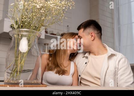 Glückliches Paar sitzt am Küchentisch, küsst sich sanft und schaut sich an. Liebe und Romantik Konzept. Hochwertige Fotos Stockfoto