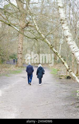 Ein älteres Paar, das im Windsor Great Park, Virginia Water, Surrey, England, Großbritannien, läuft, März 2022 Stockfoto