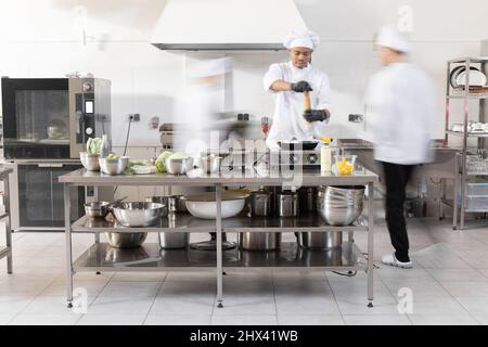 Der Koch kocht in der professionellen Küche. Köche beeilen sich und kochen aktiv Mahlzeiten für das Restaurant. Langzeitbelichtung mit bewegungsunscharfen Figuren Stockfoto