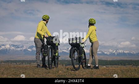 Der Mann und die Frau reisen mit Bikepacking auf gemischtem Terrain. Das Liebespaar Reise mit Zelt in der Natur mit Fahrradtaschen. Stylische Bikepacking-, Bike-, Sportbekleidung in grün-schwarzen Farben. Stockfoto