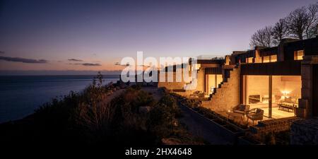 Abenddämmerung im Außenbereich, Luftansicht der beleuchteten Fenster und privater Sitzbereich und Aussichtsplattform mit Meerblick und Sonnenuntergang. Clifftops, Dorset, Portland, Stockfoto