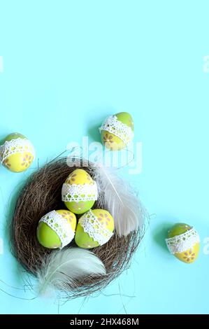 Ostereier in einem Nest mit Federn auf blauem Hintergrund. Urlaubskonzept. Stockfoto
